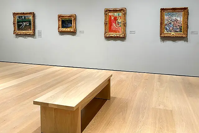 A bright gallery at the Hammer Museum with gold-framed paintings and a wooden bench